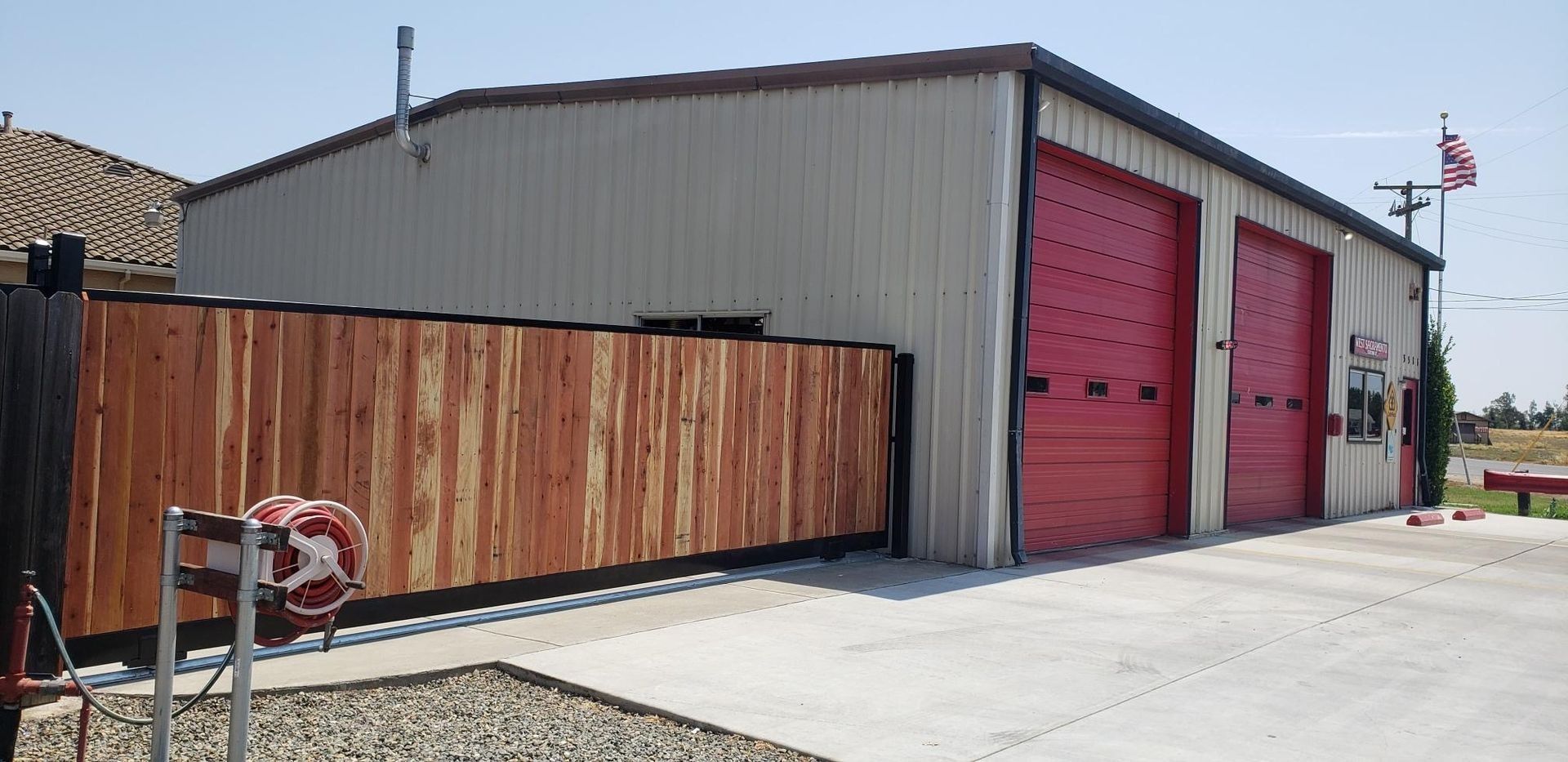 Exterior view of a tan building with two red garage doors. A wooden fence is in front.