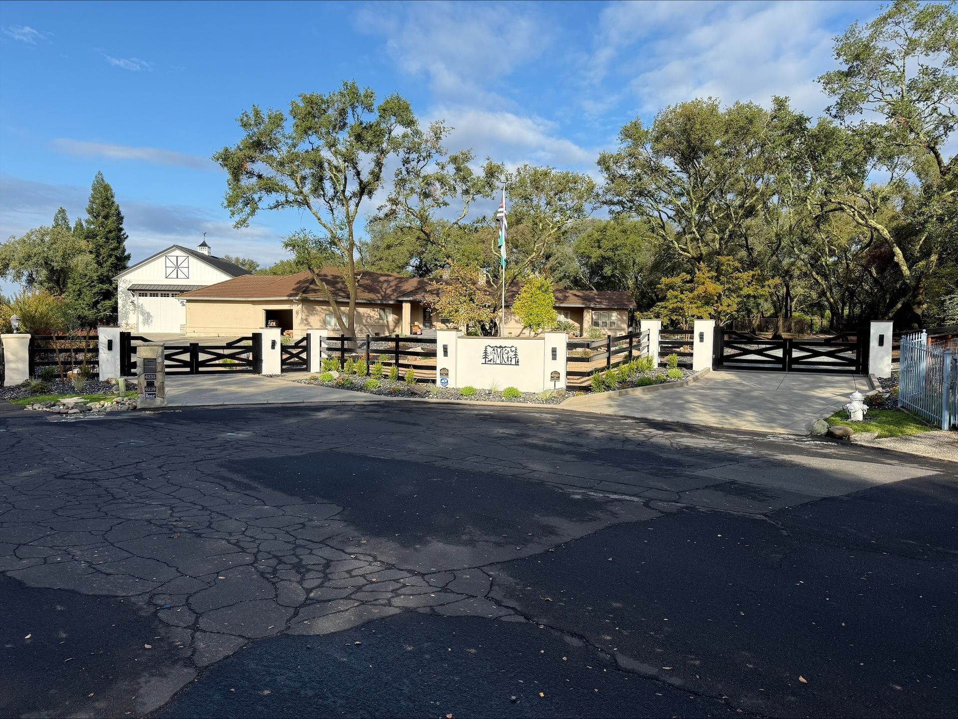 Driveway leading to a ranch-style house with black fences and large trees.