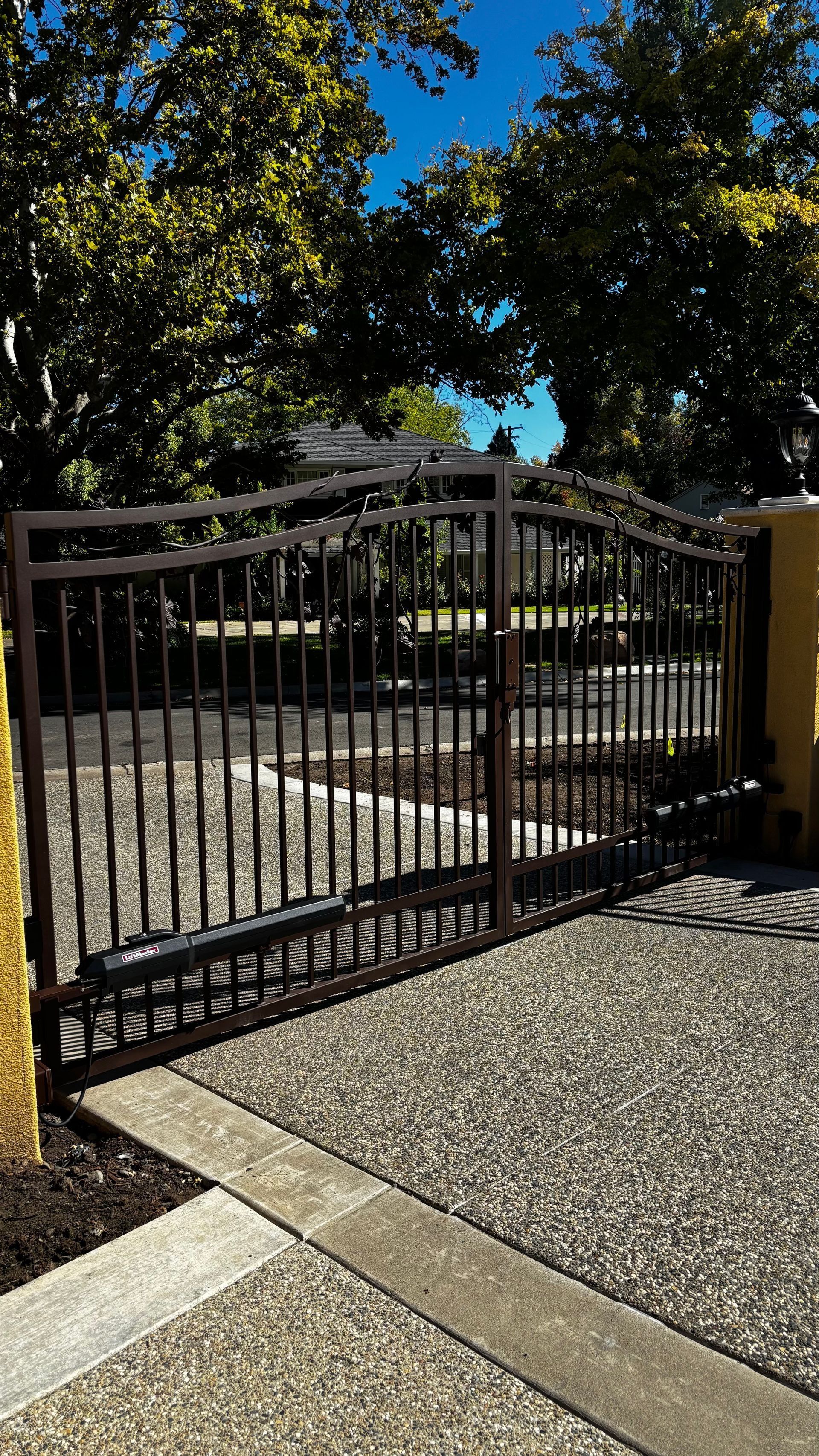 Black wrought iron gate with vertical bars set in gravel driveway.