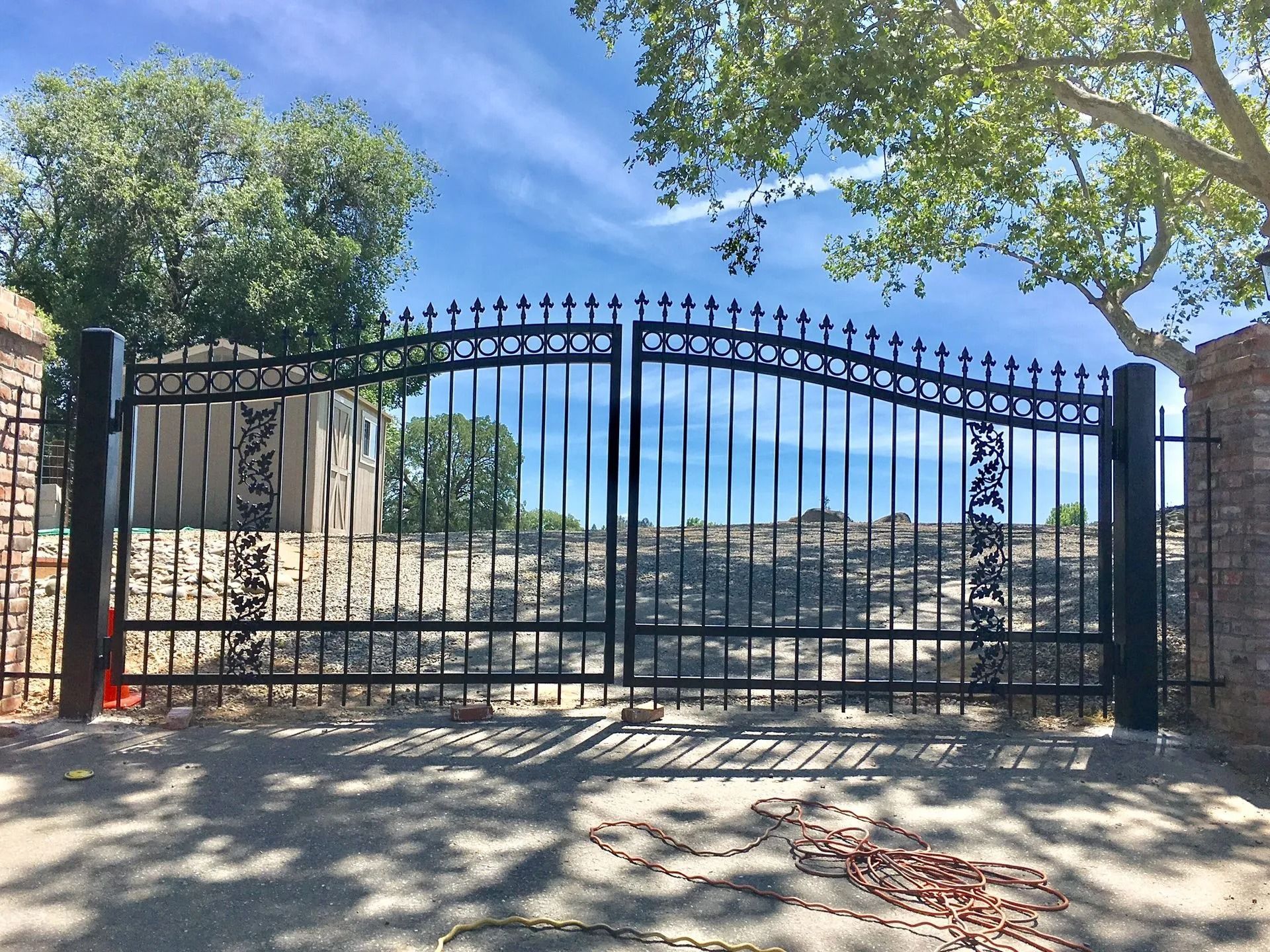 Black wrought iron gates, arched with decorative elements, are closed at the entrance to a property.