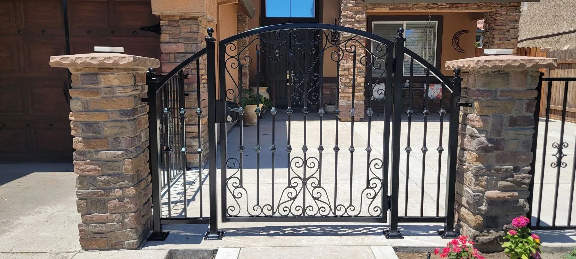 Black wrought iron gate with stone pillars at a home's entrance.