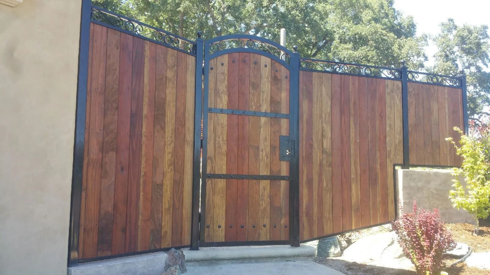 Wooden fence with a gate, black metal frame, and surrounding greenery.