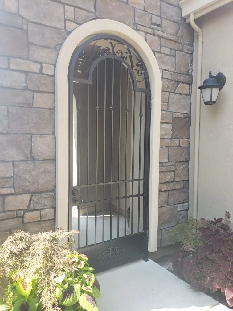 Black wrought iron gate in arched doorway with stone wall and light fixture.