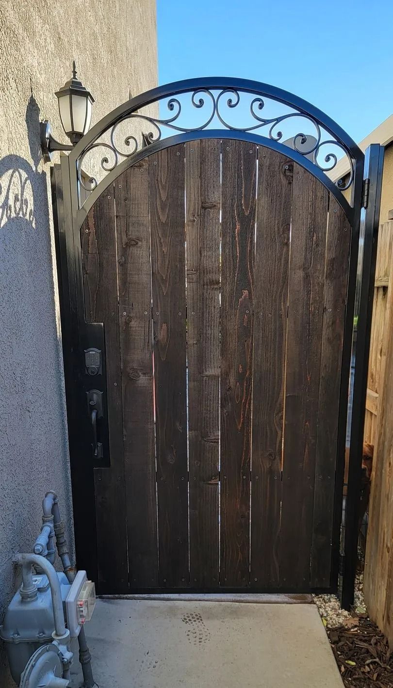 Dark wooden arched gate with black wrought iron detail and a lamp.