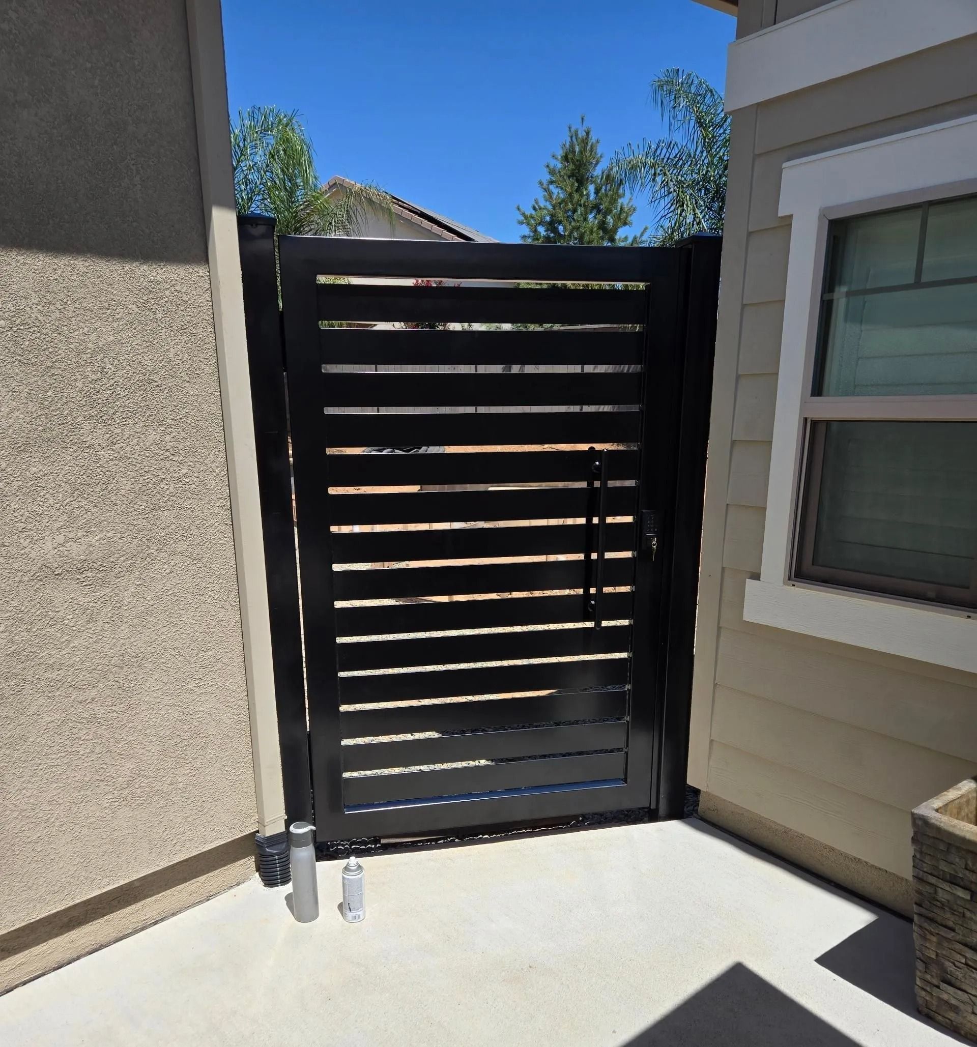 Black slatted gate in a tan-colored alcove; blue sky above.