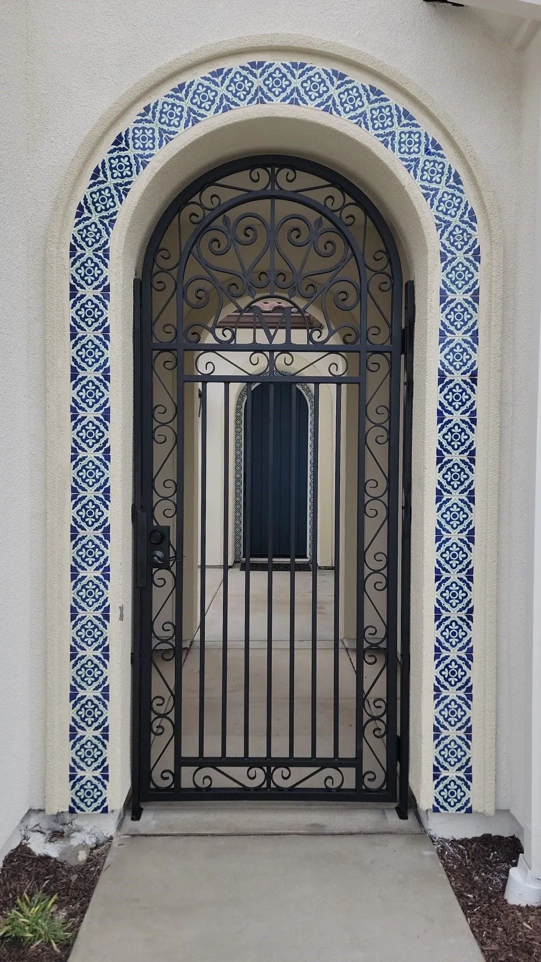 Ornate black iron gate in an arched doorway with blue and white tile trim.