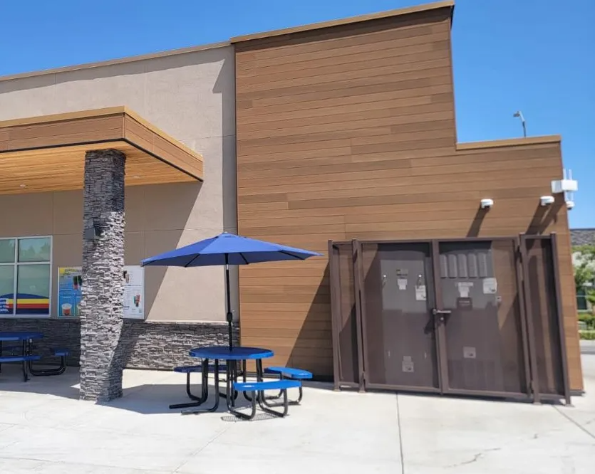 Outdoor seating area with blue picnic table, umbrella, and a brown security cage.
