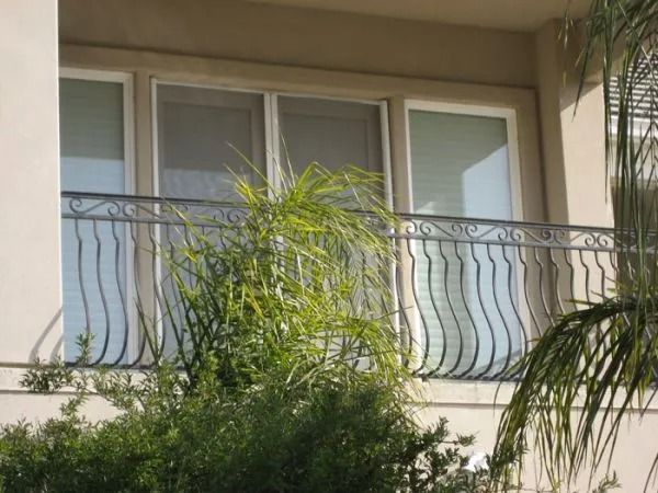 Balcony with wavy metal railing, windows, and greenery.