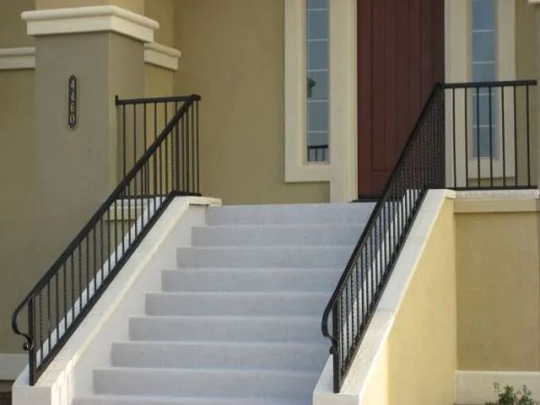Exterior concrete steps with black railings leading to a doorway. Beige walls and a dark brown door.