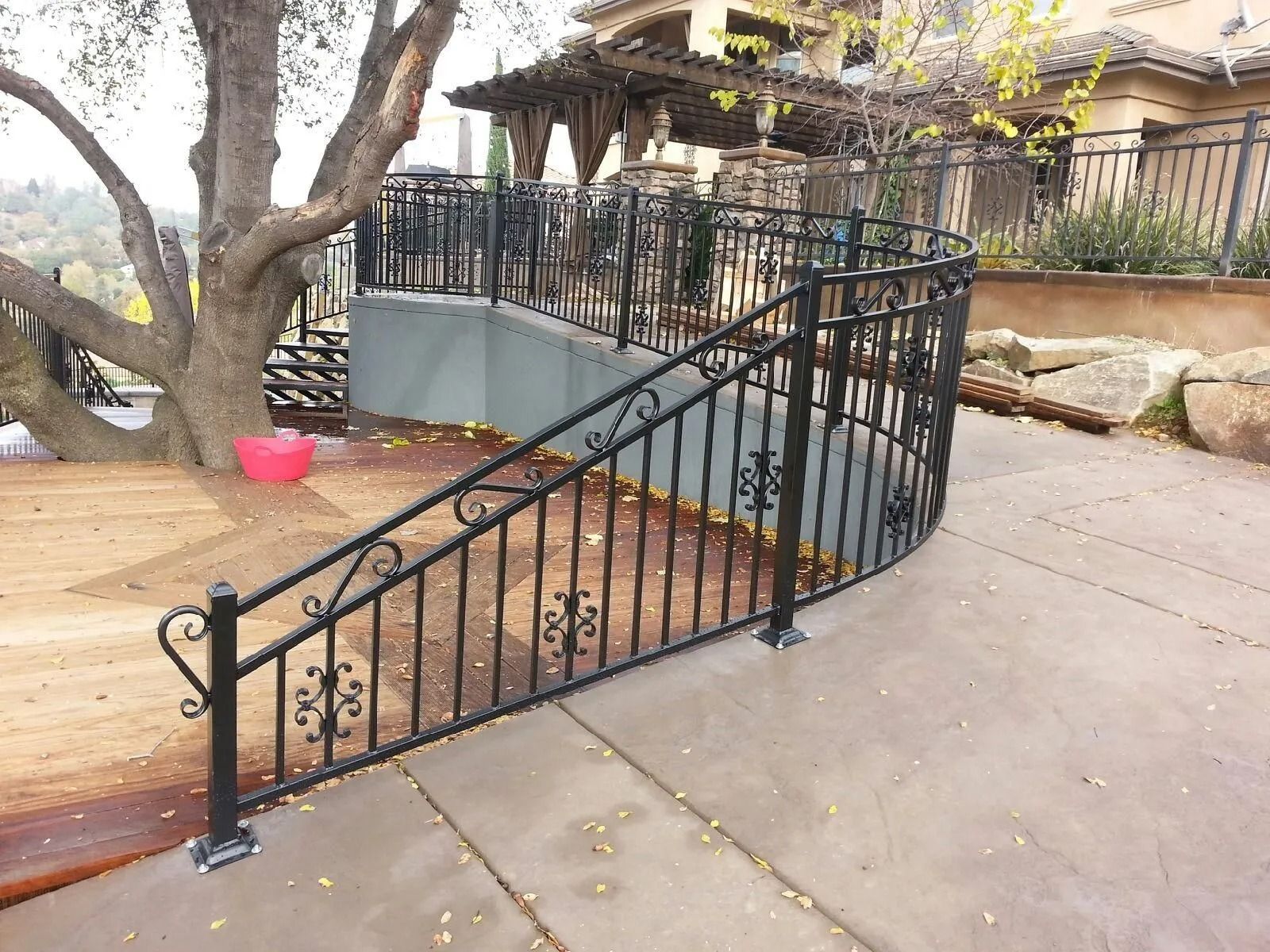 Black wrought-iron railing curves around outdoor steps, beside a tree and patio with a view.