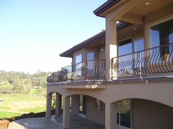 Beige house with wrought iron railings and arched columns, overlooking a green landscape.