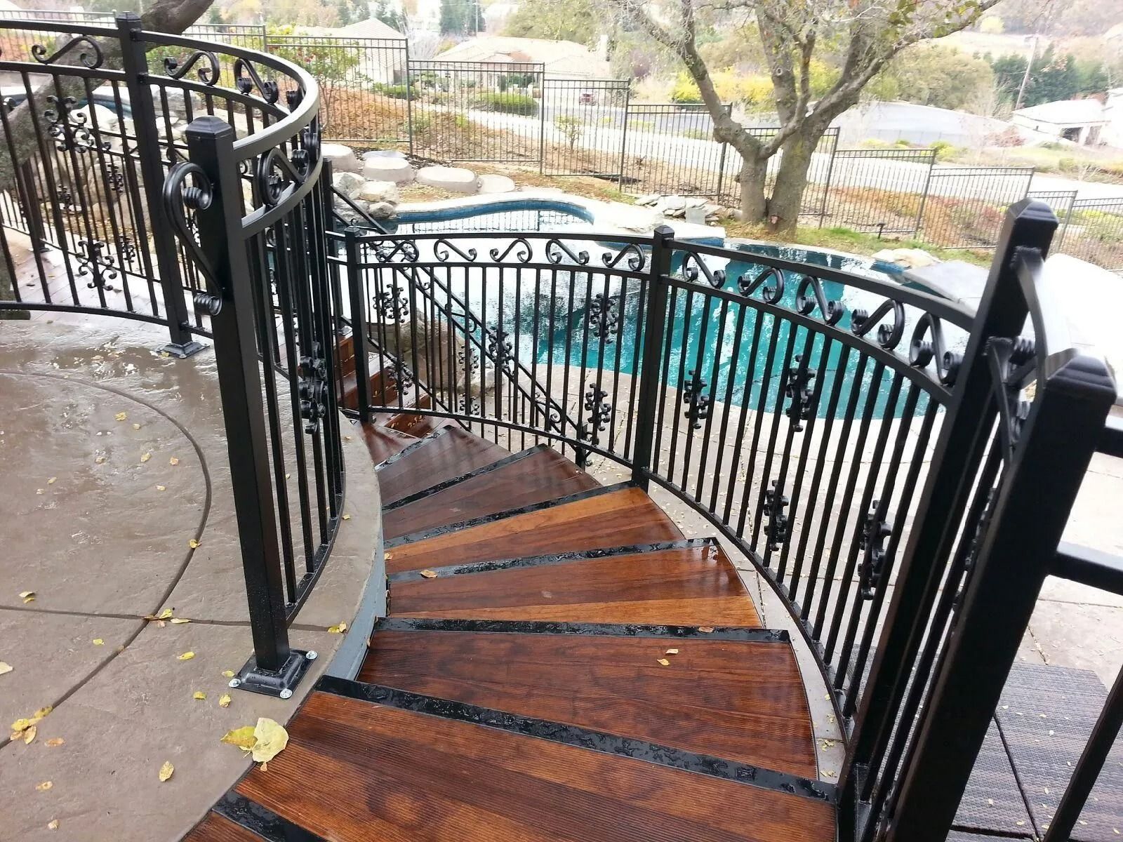 Curved wooden staircase with black iron railing overlooking a pool.