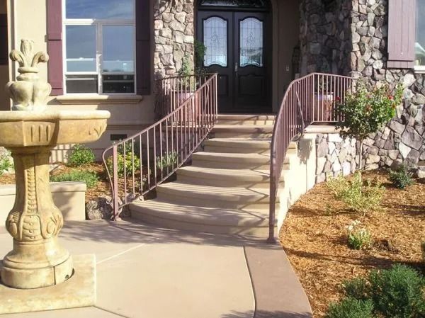 Exterior of a house with stone siding, concrete steps, and a decorative fountain. Brown railing.