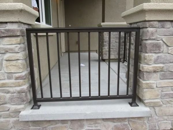 Brown metal railing in front of a porch with stone columns and a concrete base.