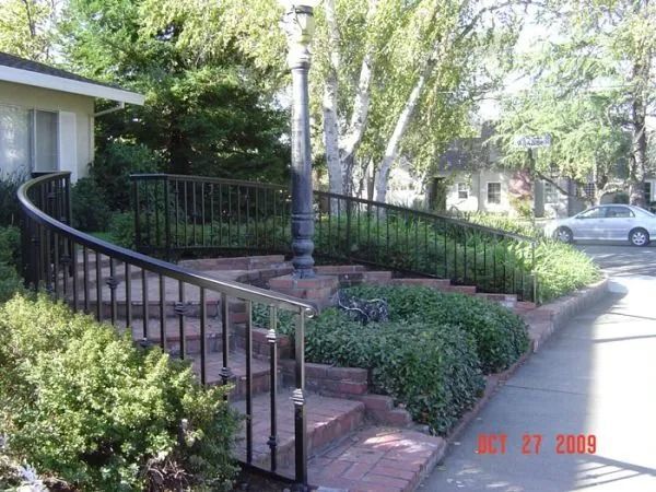 Brick stairs with black railing, street lamp, and landscaping.