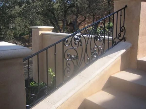 Black wrought-iron railing with ornate scrollwork along tan stone steps, leading to a home's entryway.