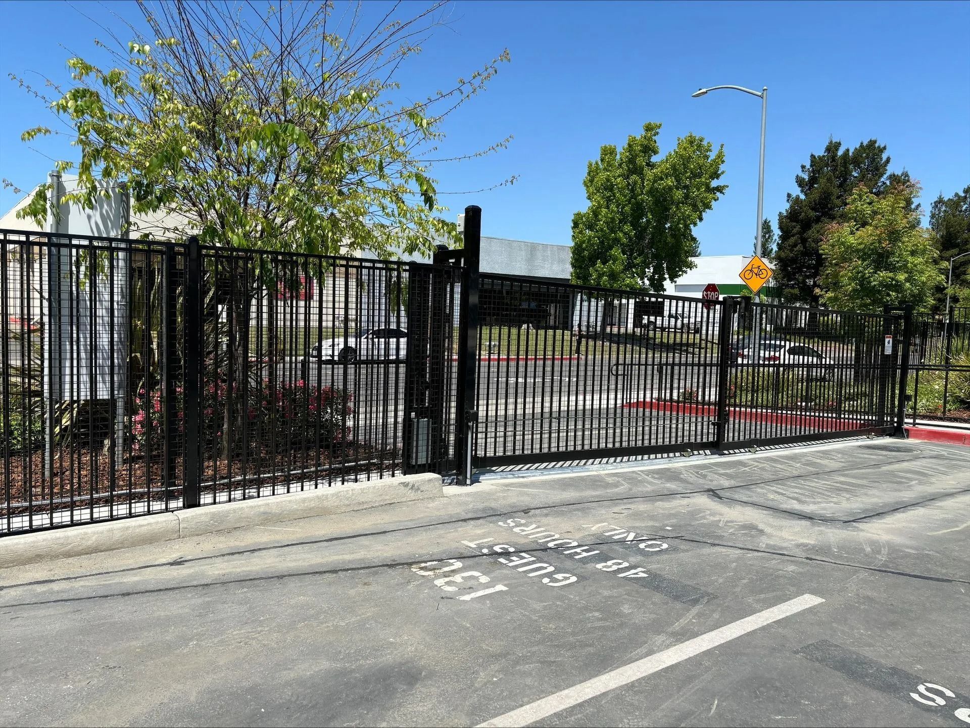 Black metal gate, fence, and concrete base in a parking lot on a sunny day.
