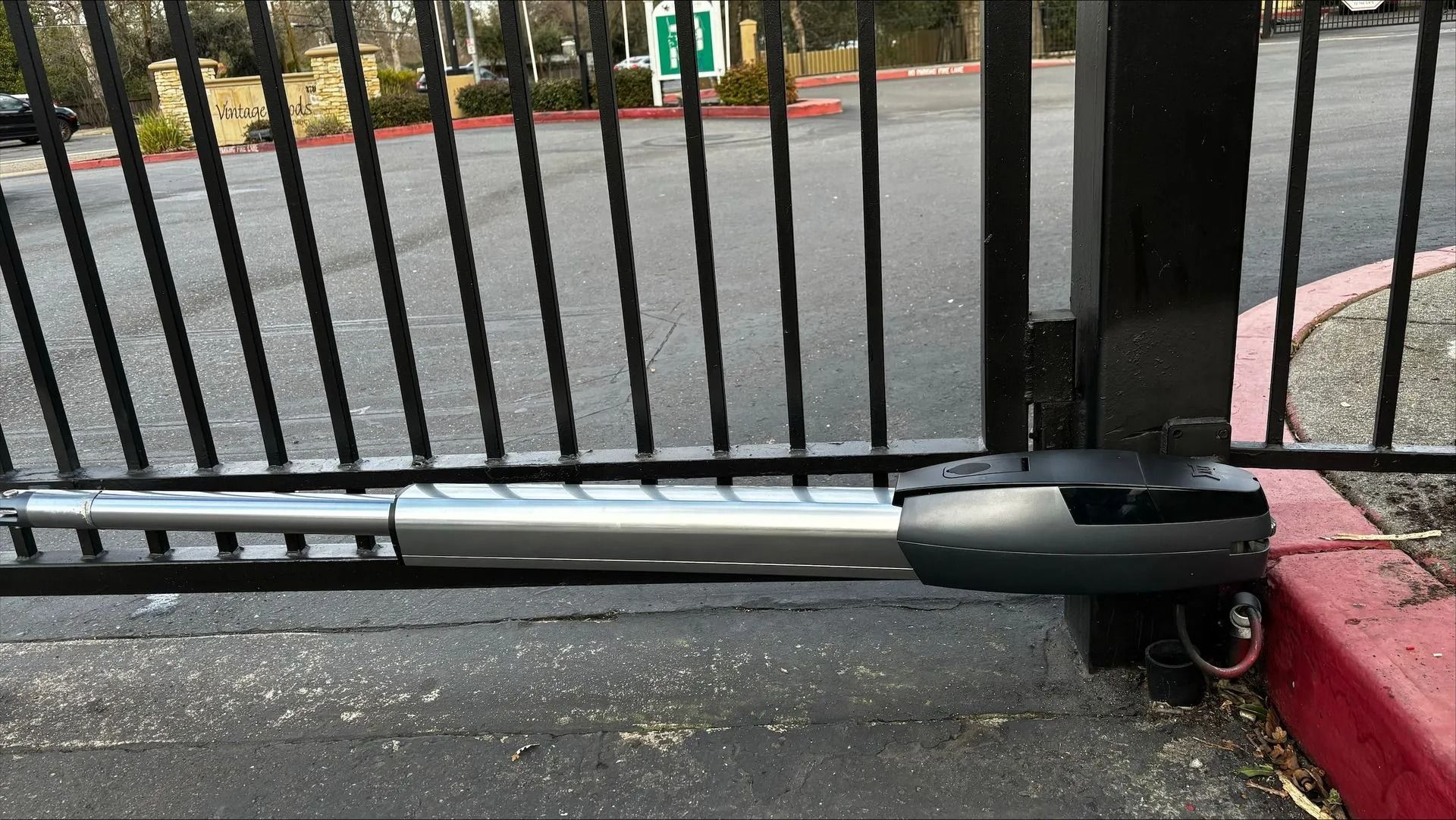 Gate opener on a black wrought-iron gate, attached to a red curb.