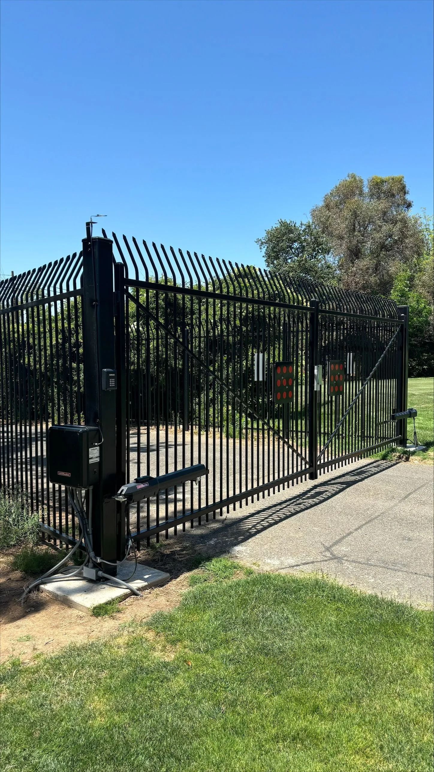Black metal security gate on a concrete pad, with tall spikes on top and an automatic opener.