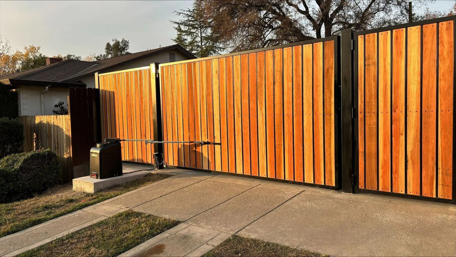 Wooden driveway gate with black metal frame; brown wooden panels.