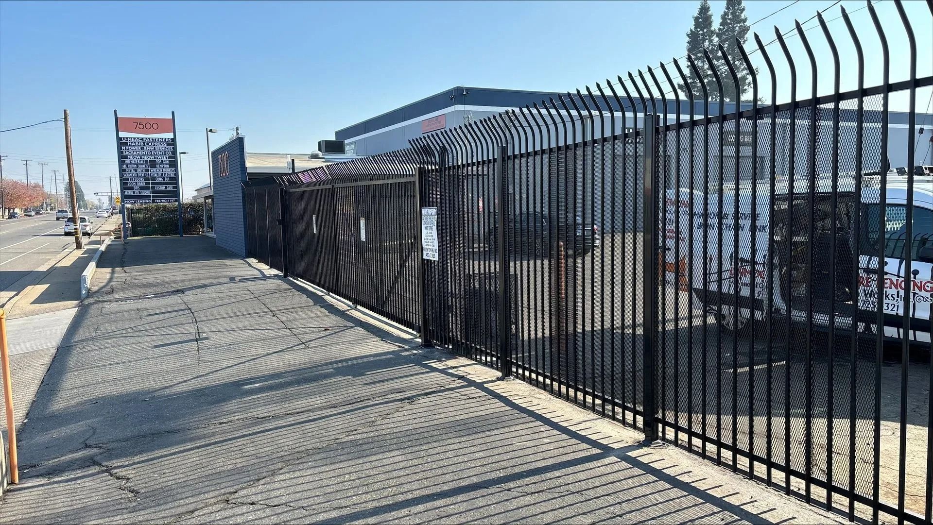 Black metal fence with pointed tops surrounds a business. Gravel pathway in front.