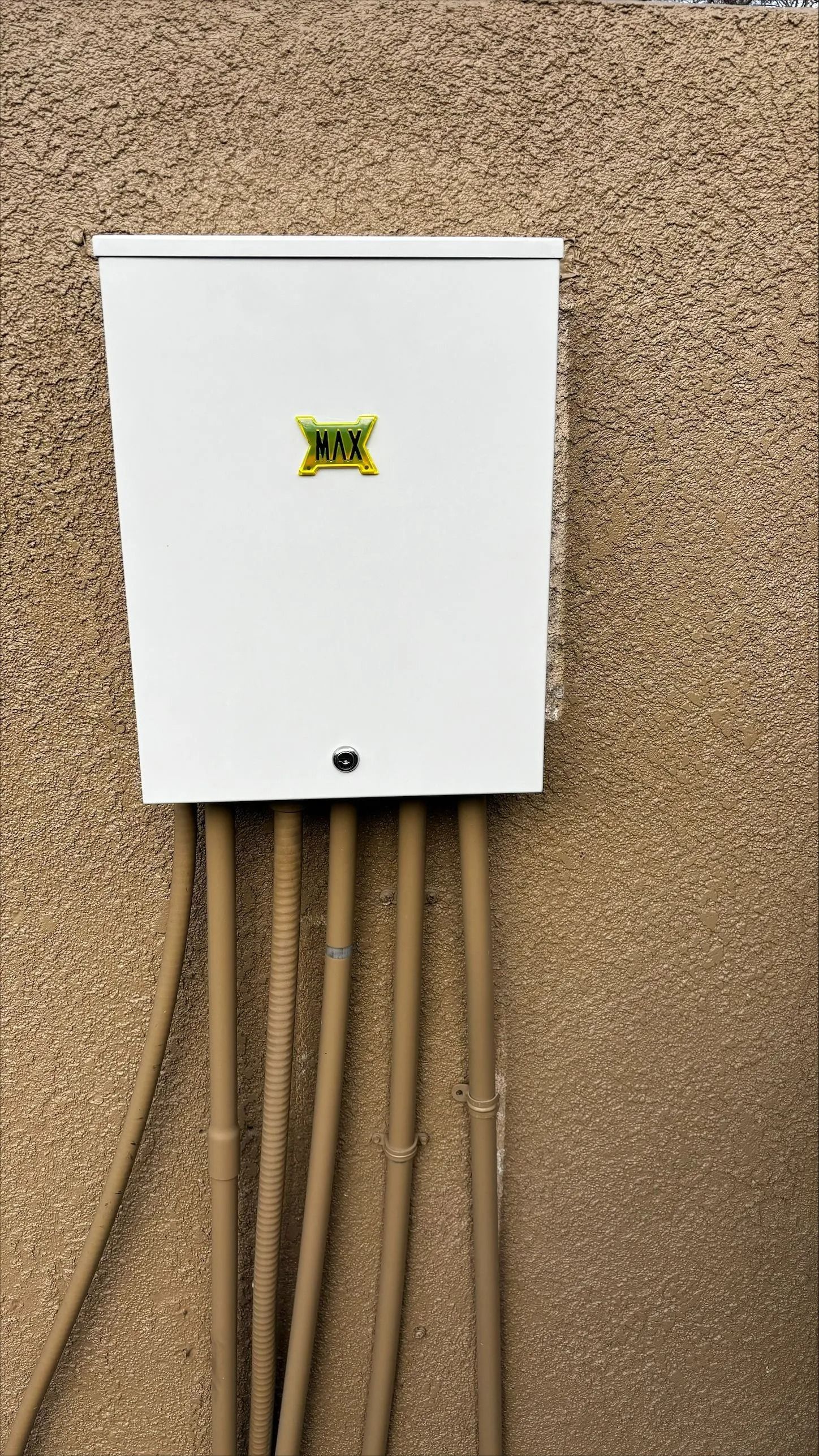 White electrical box on textured beige wall with brown conduits.