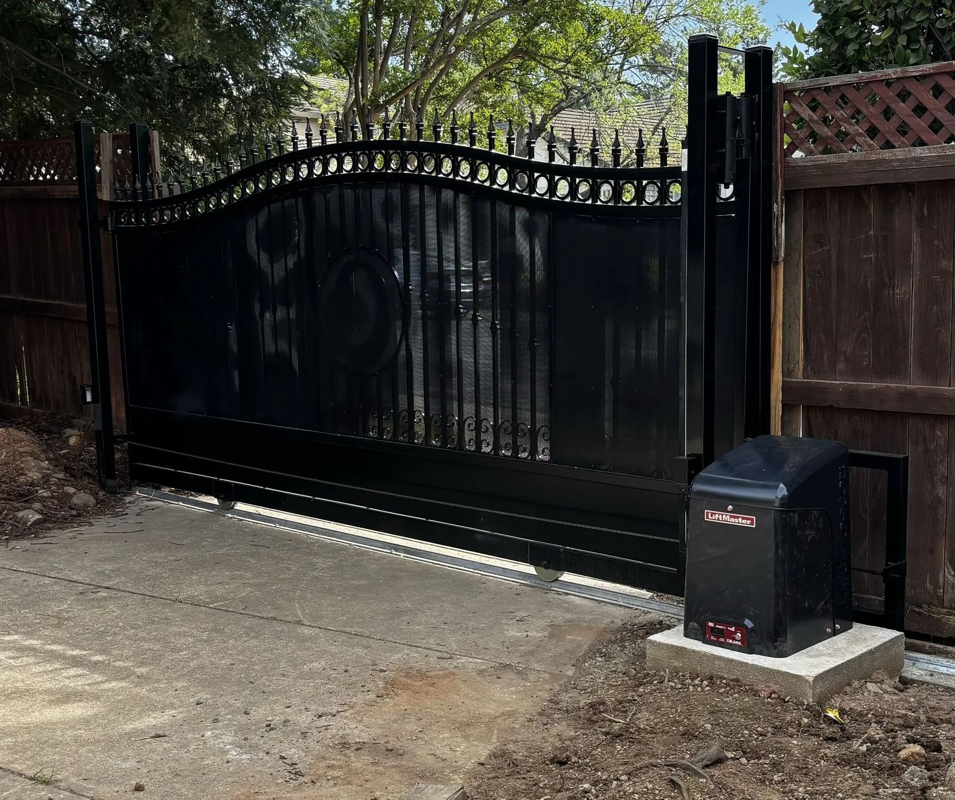Black wrought iron sliding gate with automatic opener on a concrete driveway.