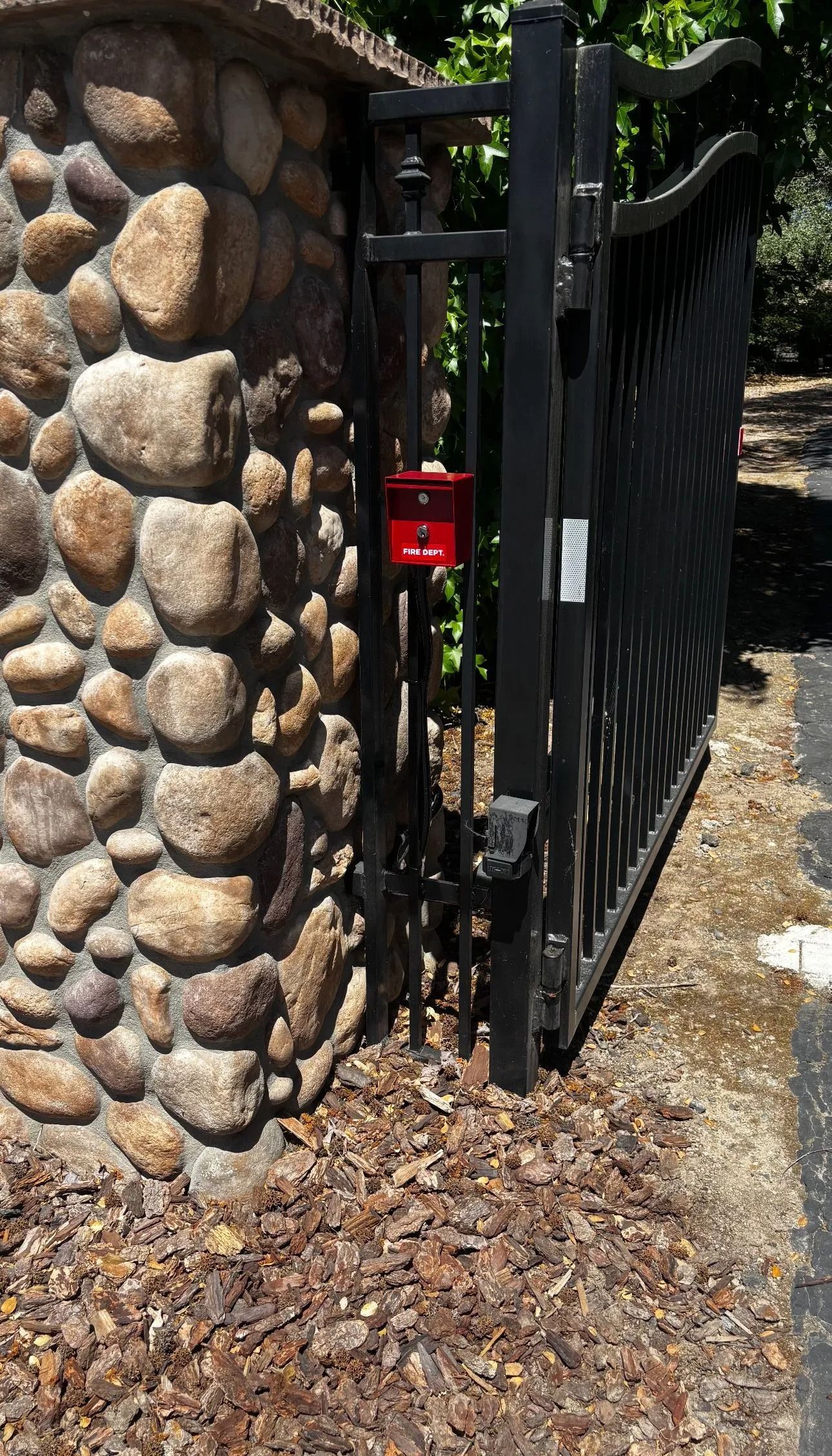 Black wrought iron gate attached to a stone column with a red mailbox.