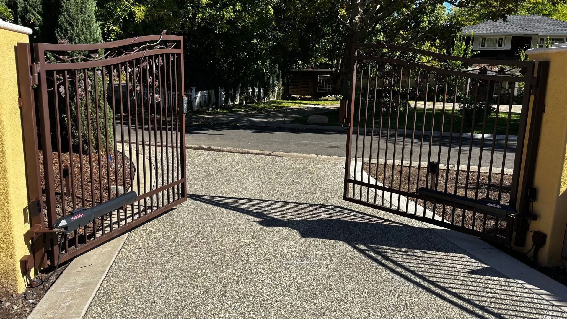 Brown metal driveway gates, open, with a concrete drive leading to a house.