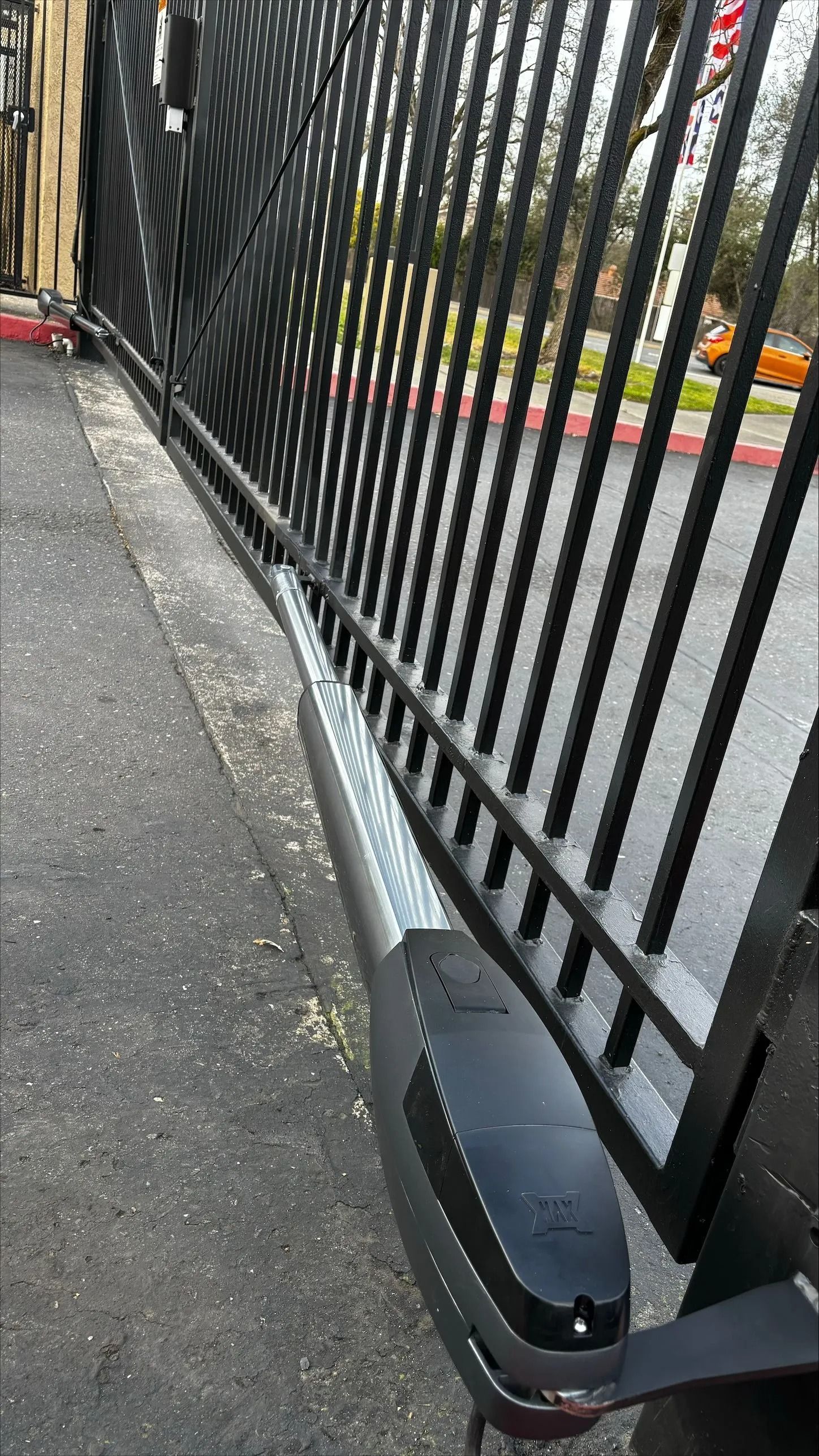 Automatic black metal gate and opener on a paved driveway.
