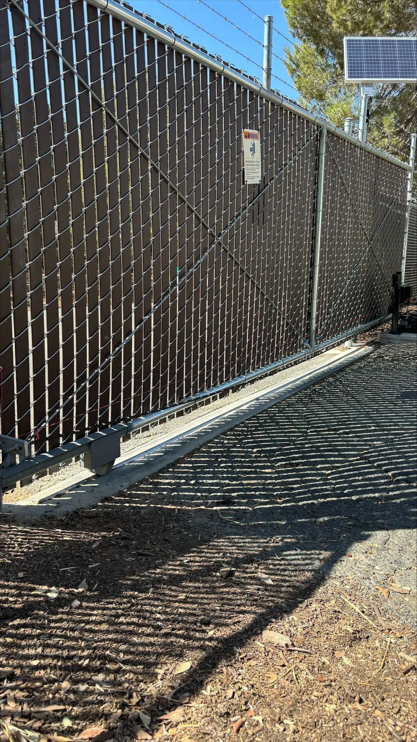 A dark fence with slats blocks entry. Shadows cast on the ground.