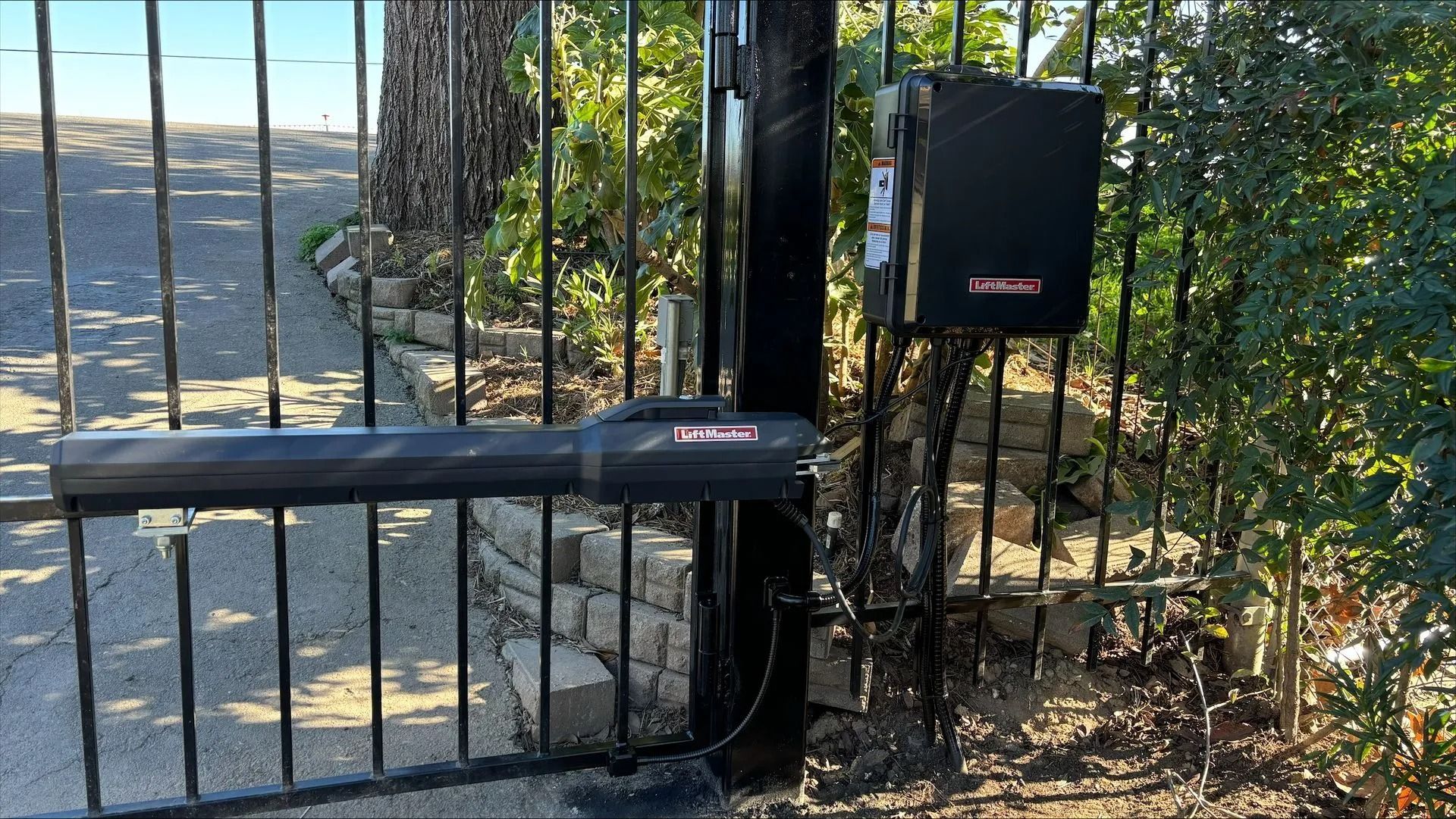 Black automated gate with opener and control box mounted to a post.