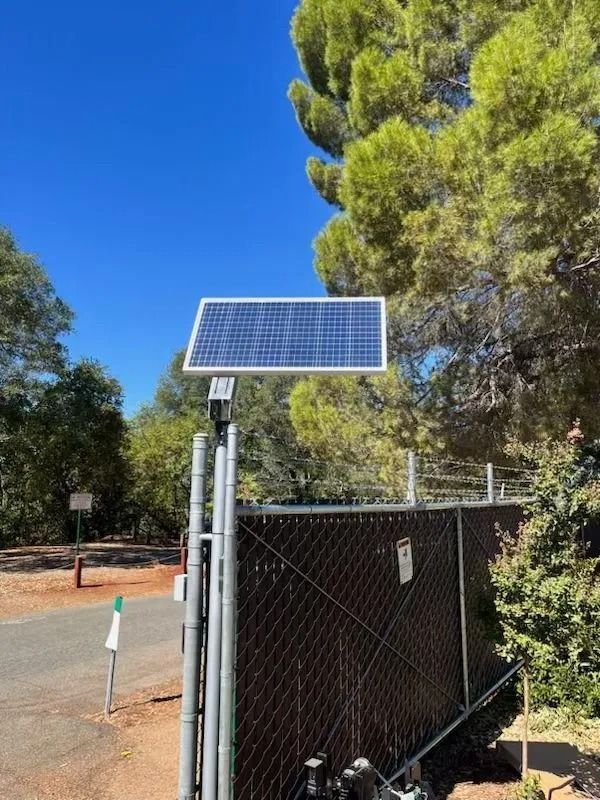 Solar panel on a gate, providing power. Blue sky and trees in the background.