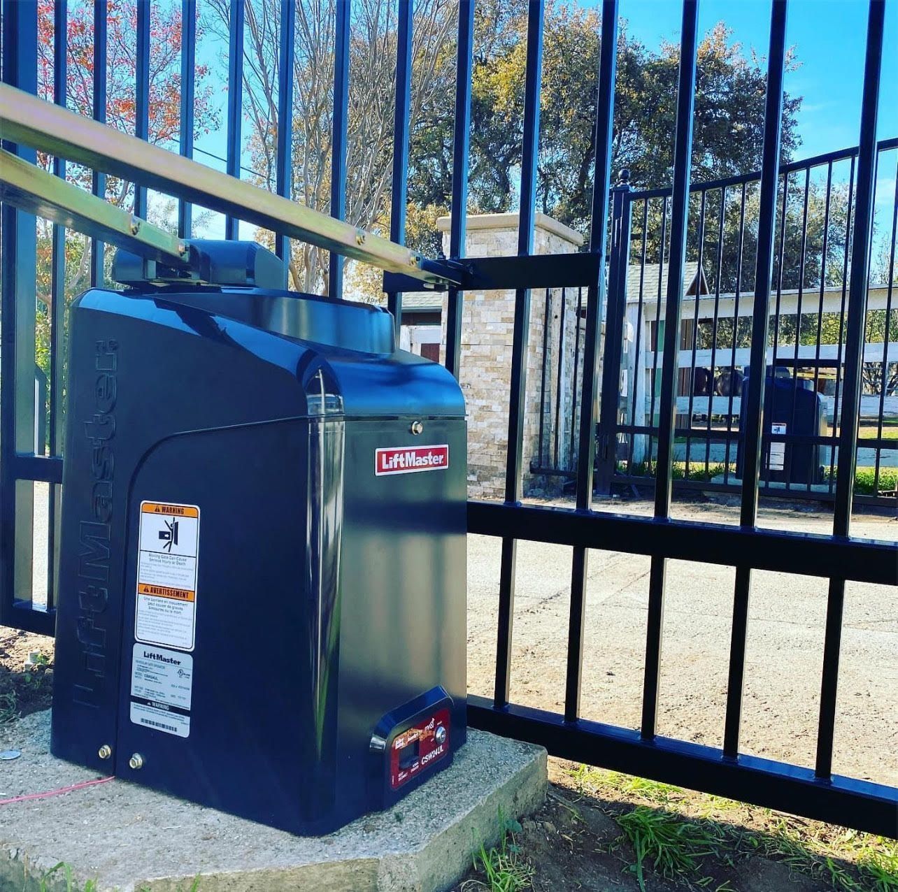 Black automatic gate opener with attached metal arm on a black metal fence.