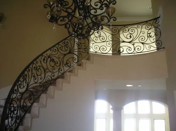 Ornate wrought iron railing on curved staircase. A chandelier hangs above.
