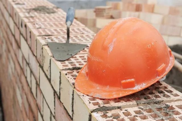 Orange hard hat and trowel rest on a brick wall under construction.