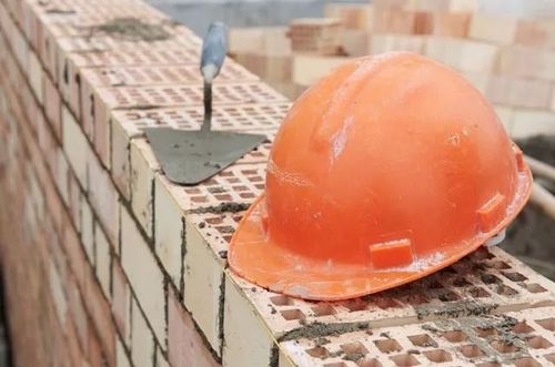 Orange hard hat and trowel rest on a brick wall under construction.