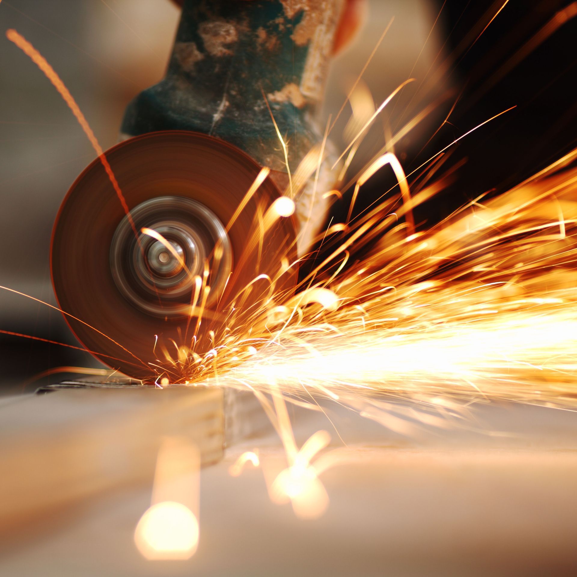 Sparks fly from a metal grinder, cutting a metal bar.