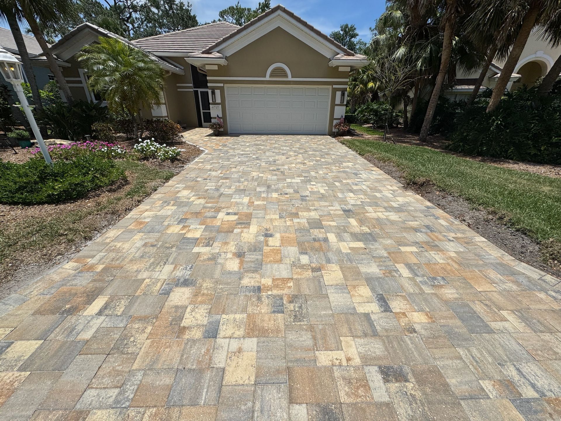 Driveway paved with multi-colored rectangular blocks leading to a beige house with a white garage door.