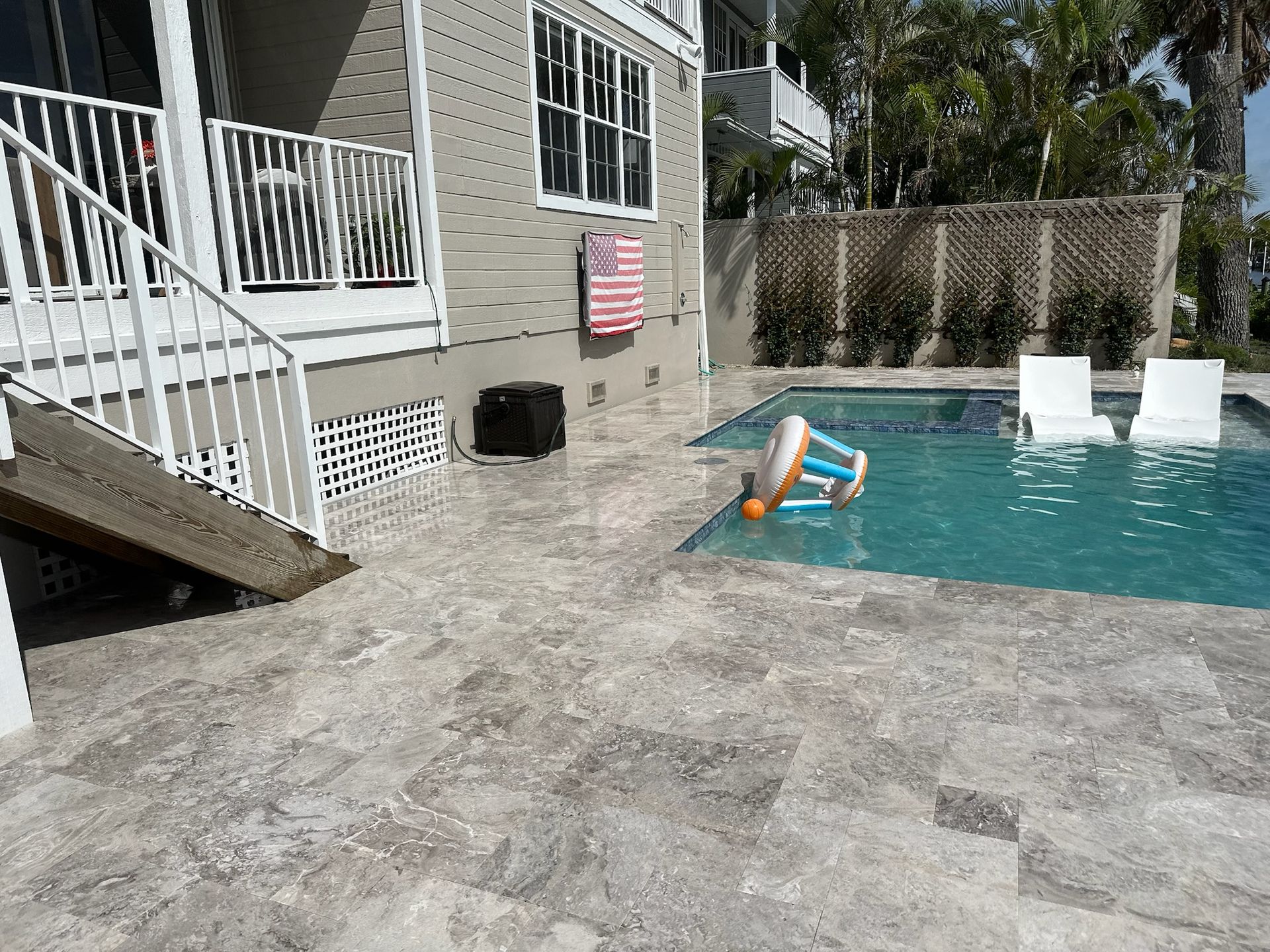 Back patio with pool. White railing and stairs, basketball hoop in pool, white chairs. Gray tile flooring.