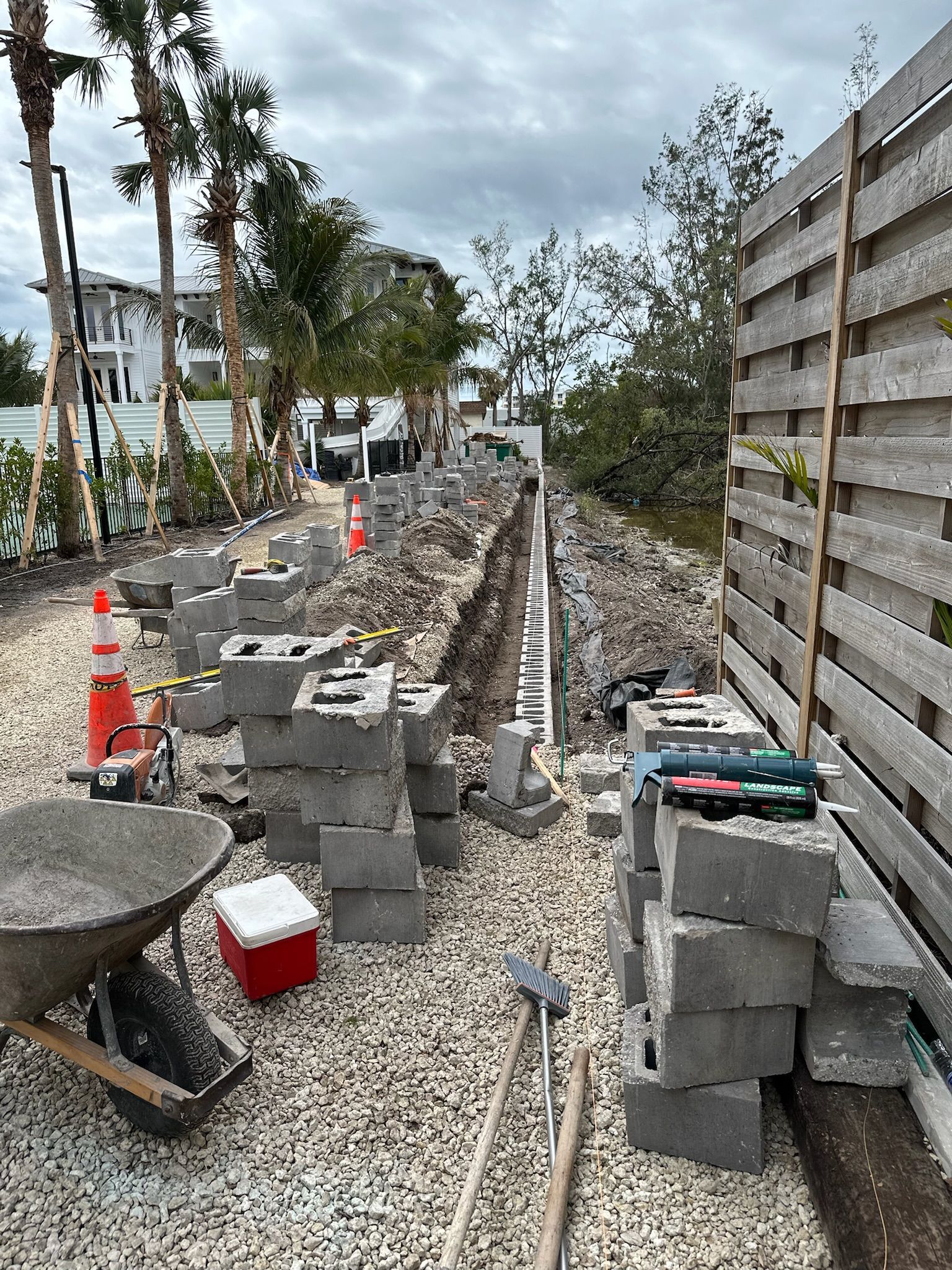 Construction site with concrete blocks, gravel, wheelbarrow, and wooden fence.