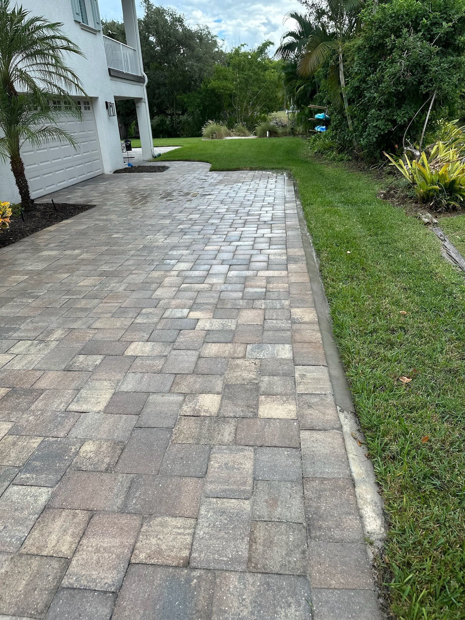Brick driveway next to a patch of green grass, leading up to a white house.