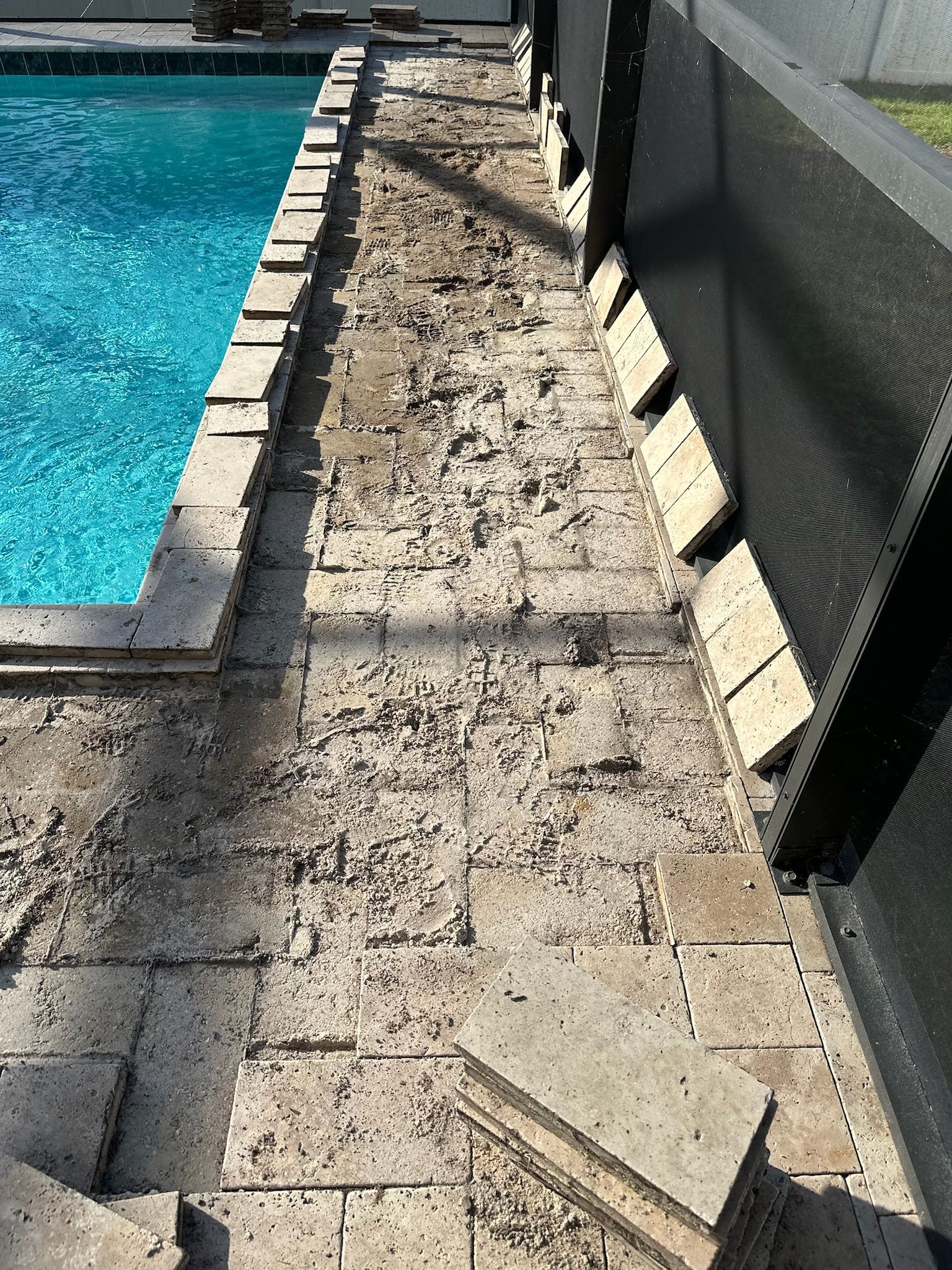 Poolside area with damaged, weathered paving stones and pool safety screen.