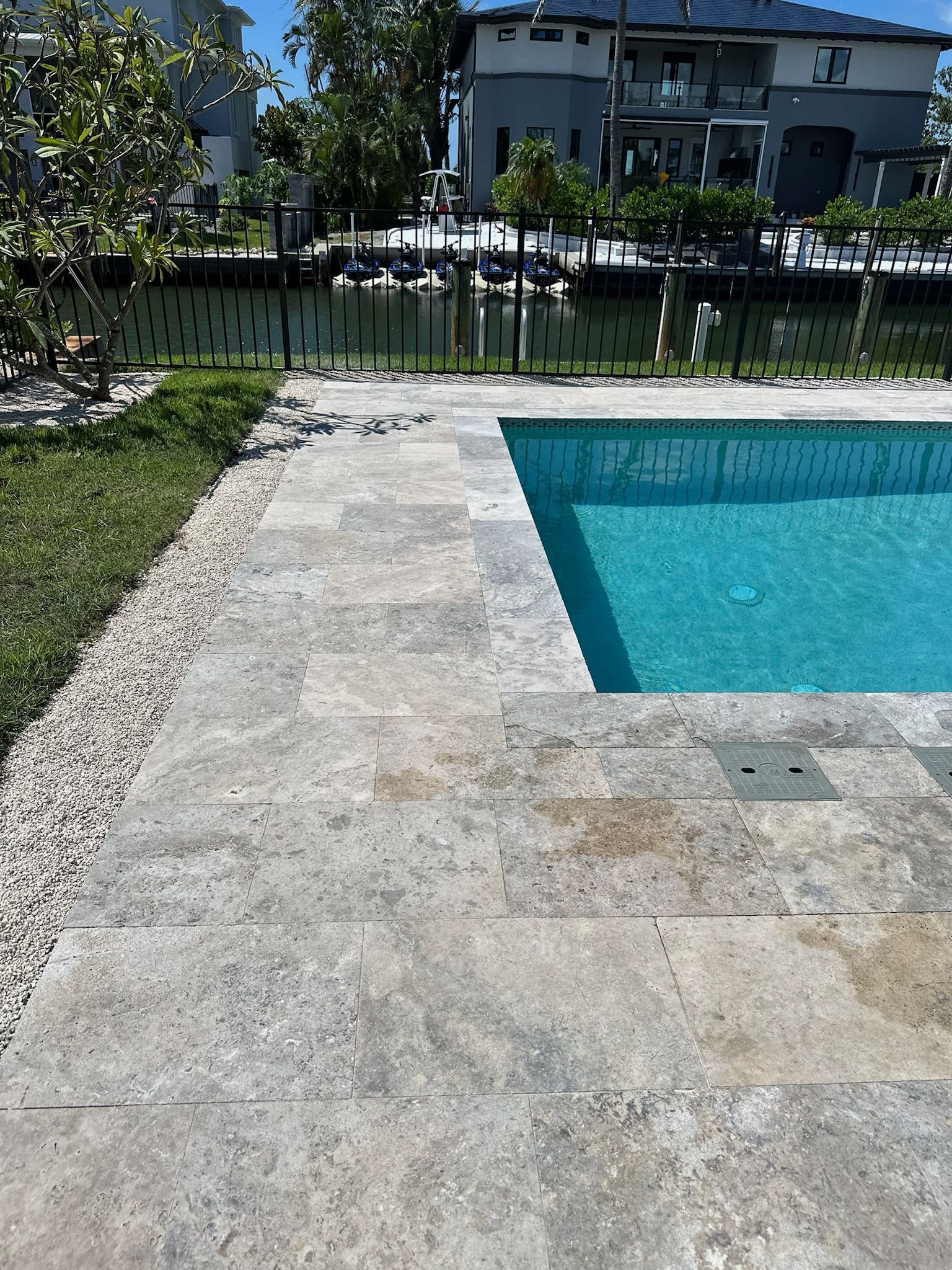 Poolside patio with travertine tiles and small gravel border, pool water turquoise.