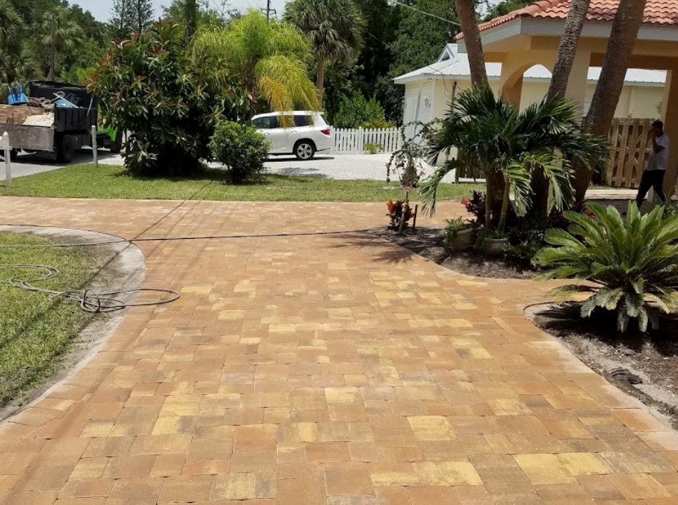 Brick driveway leading to a house, with a truck, car, and landscaping.