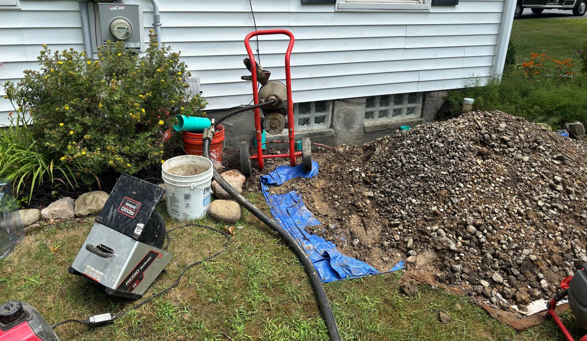 Exterior view of a house with construction equipment and gravel pile; likely foundation work.