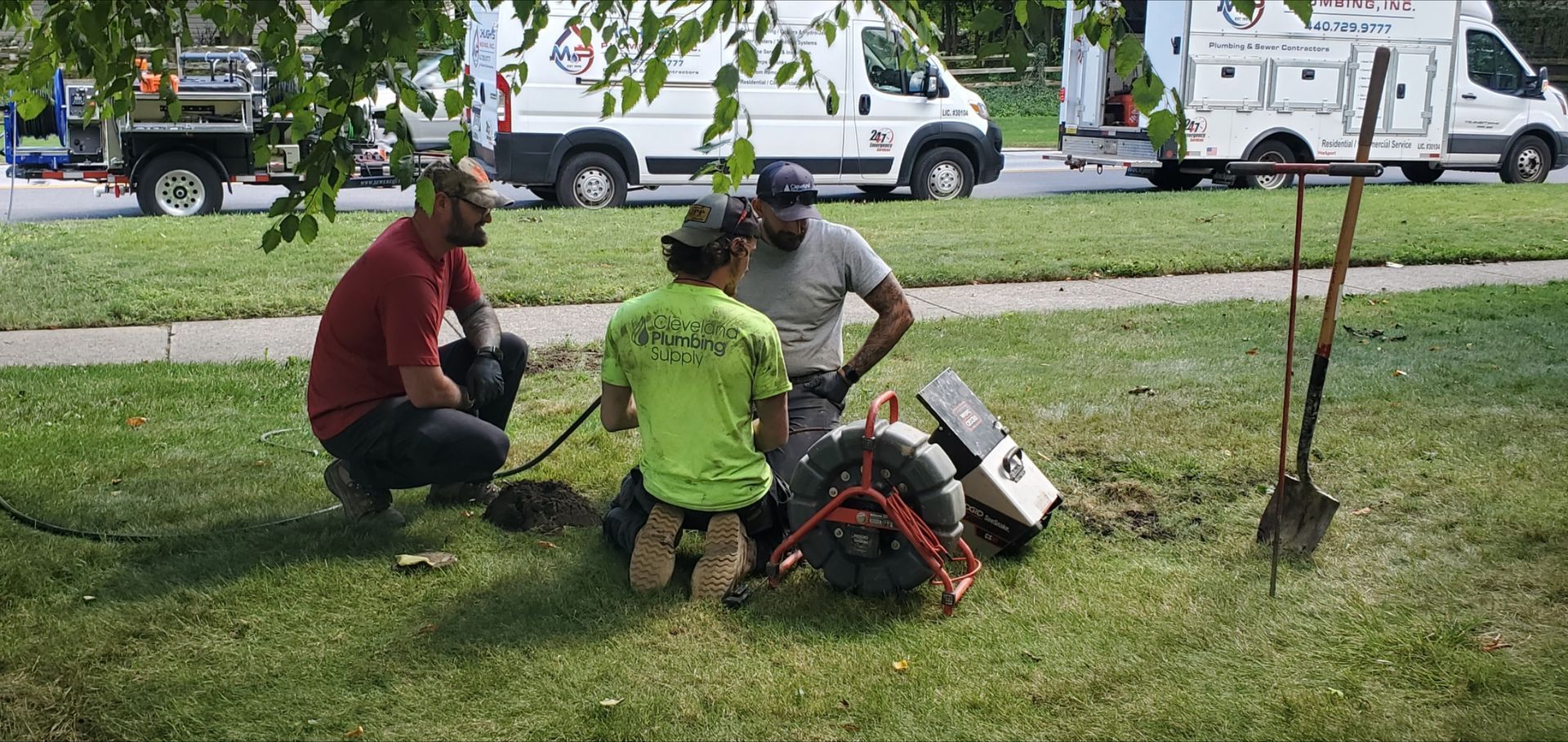 Three utility workers examining equipment in a grassy area with vans in the background.