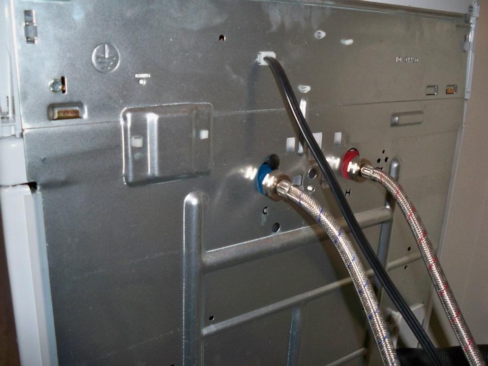 Back of a washing machine showing water supply hoses connected.