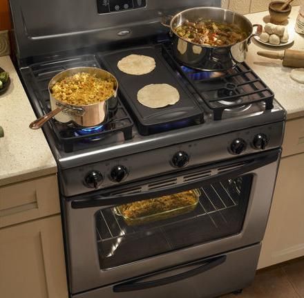 Stainless steel stove with pots cooking food and griddle with tortillas. Oven door open.