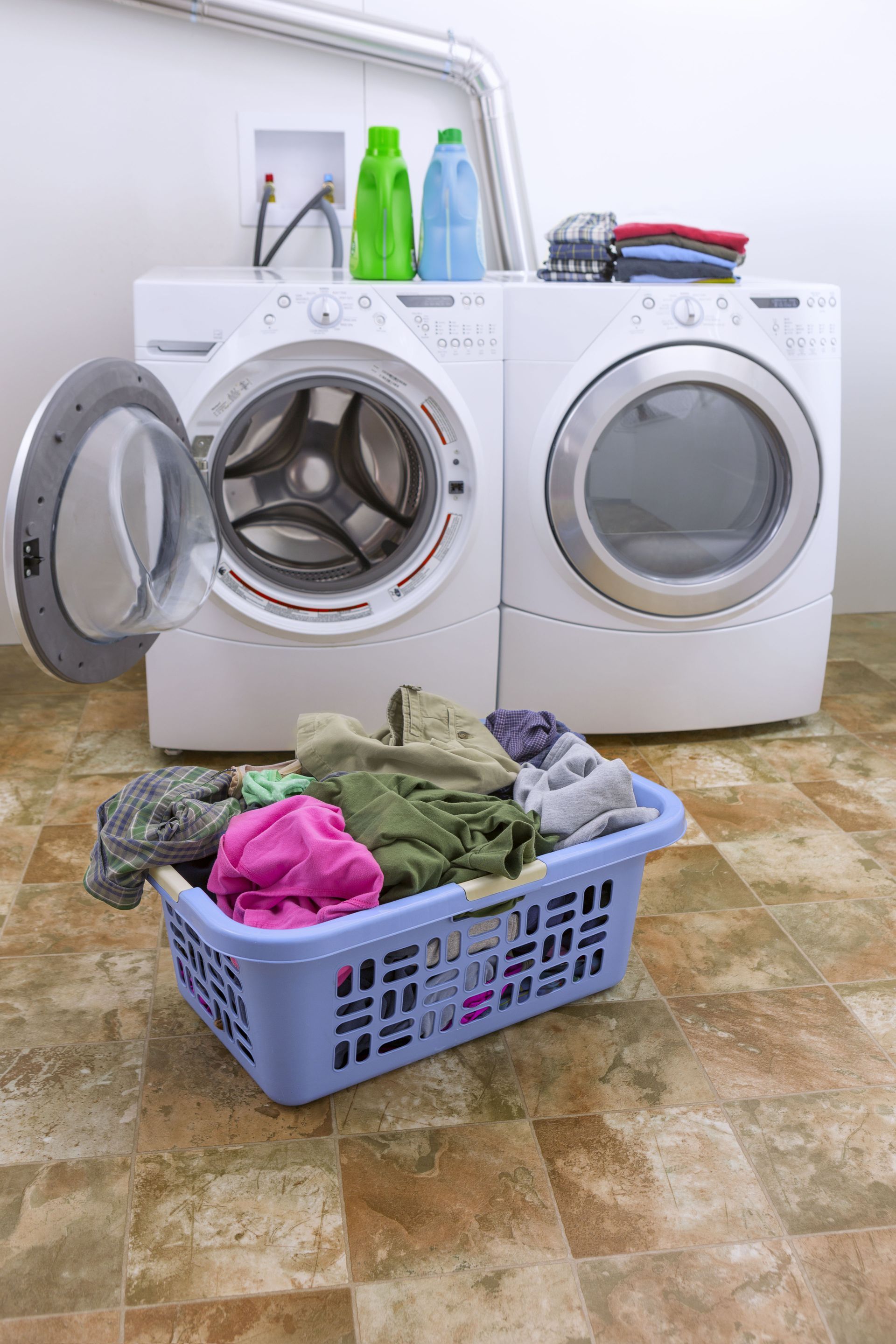 Laundry basket full of clothes in front of a washing machine and dryer, laundry room.